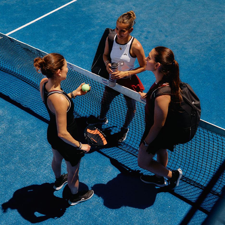 Agostina Bigotti and two fellow players in CRIVIT sportswear, standing together by the padel net on a blue court after the match.