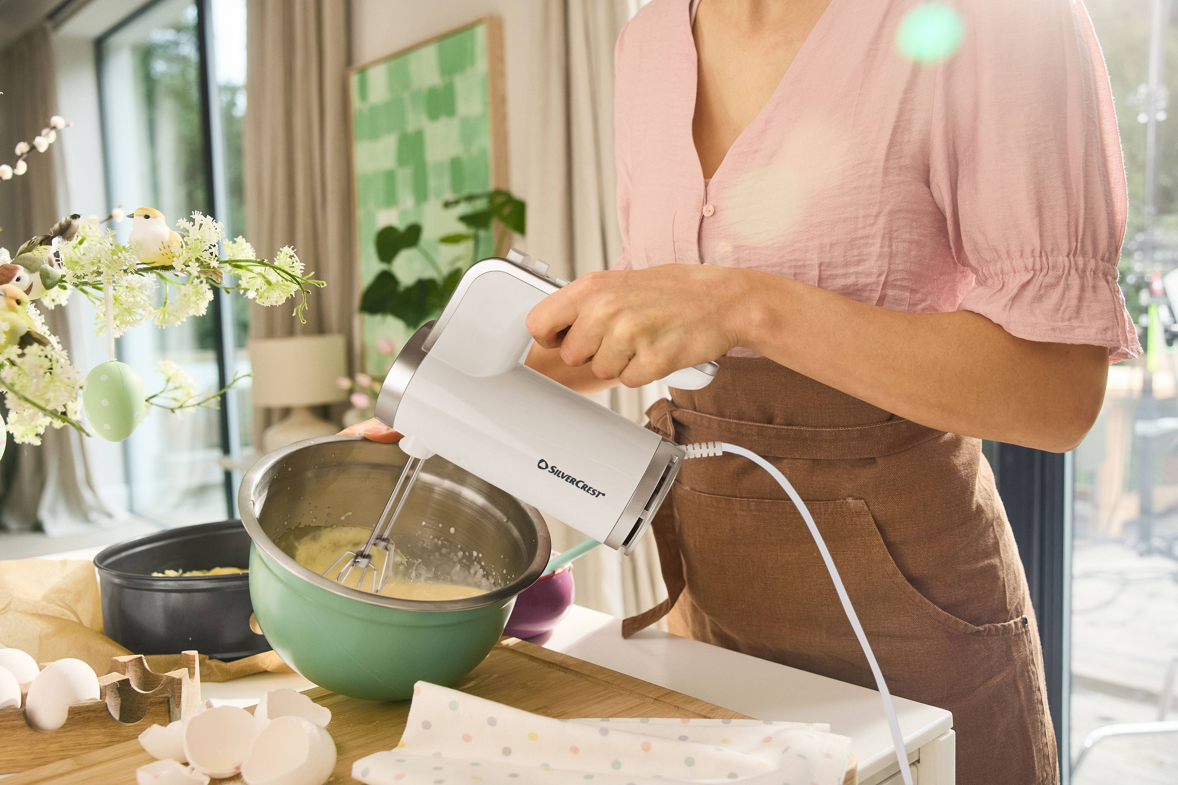 Woman using a SilverCrest hand mixer to blend ingredients in a bowl.
