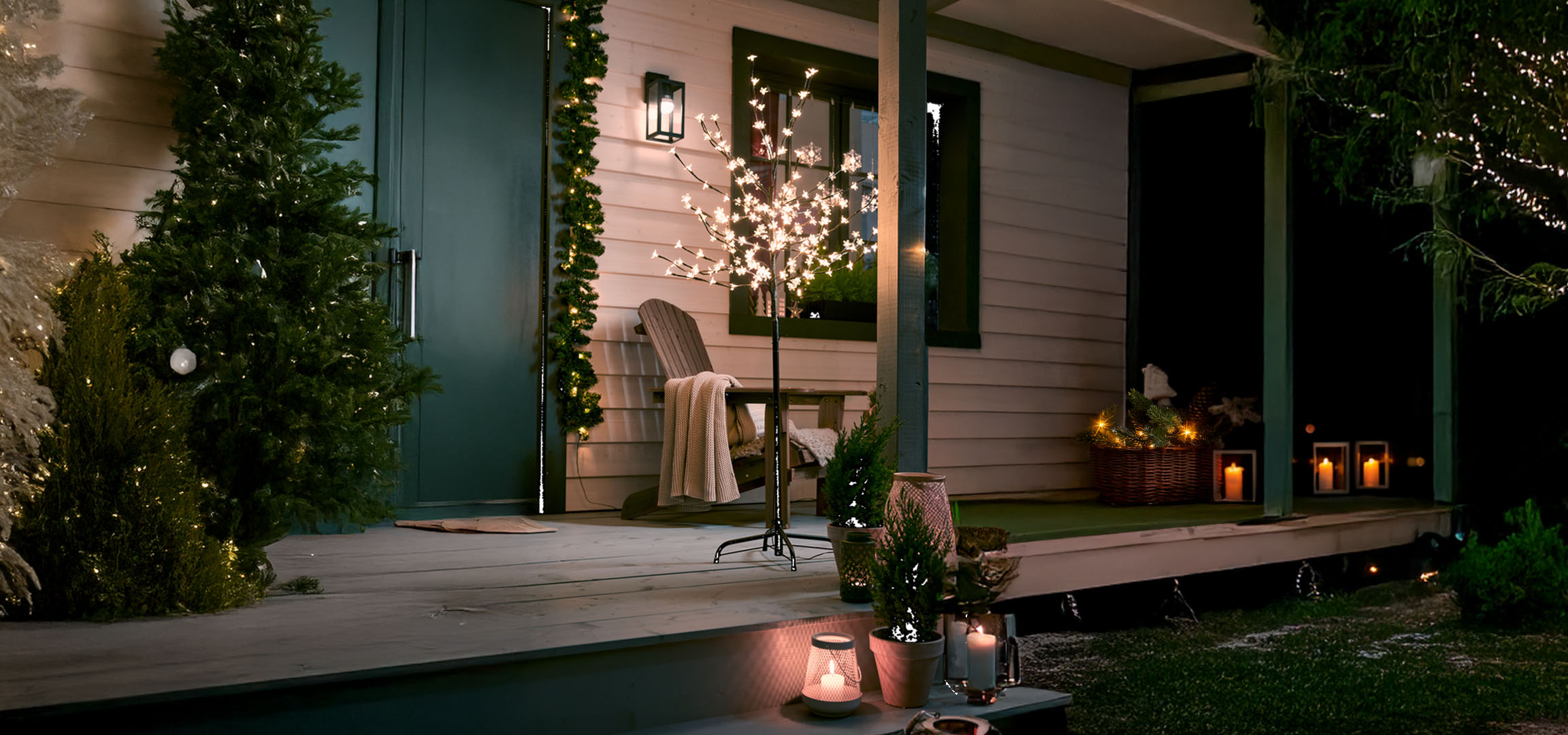 Home porch decorated with Christmas lights, illuminated trees, and candles.