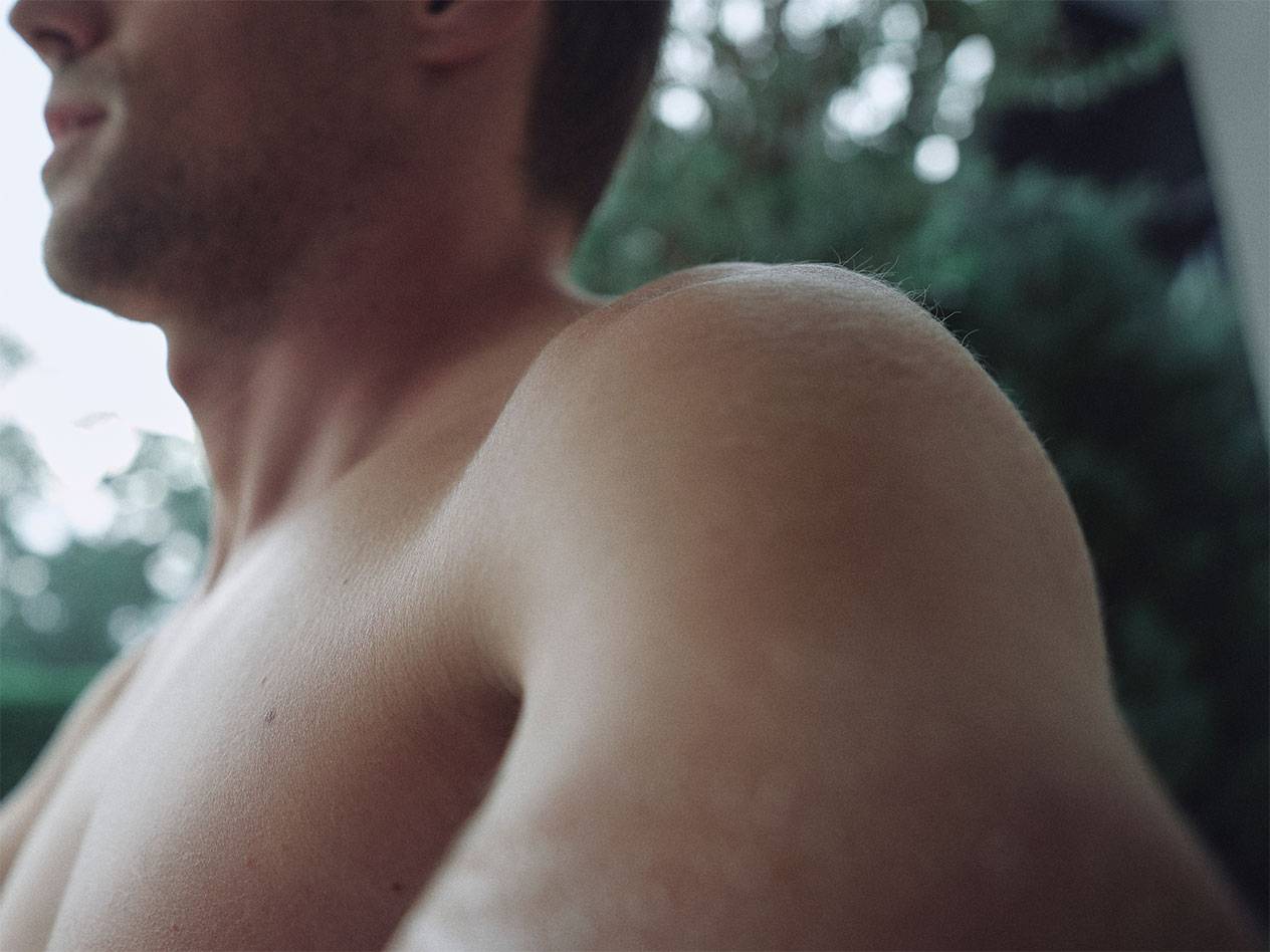 Close-up of a man's shoulder and neck, with a blurred green background.