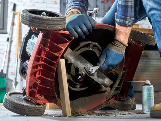 Man maintaining a lawnmower, tightening the blade with a wrench.