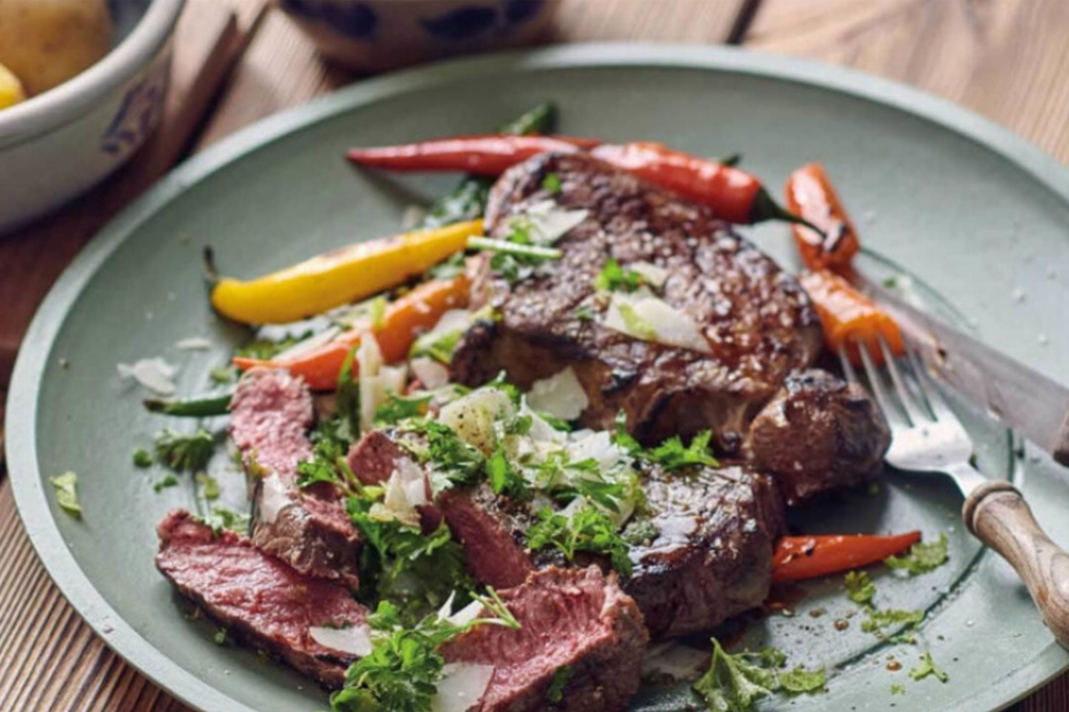 Grilled steak with peppers, fresh herbs, and shaved cheese on a green plate.