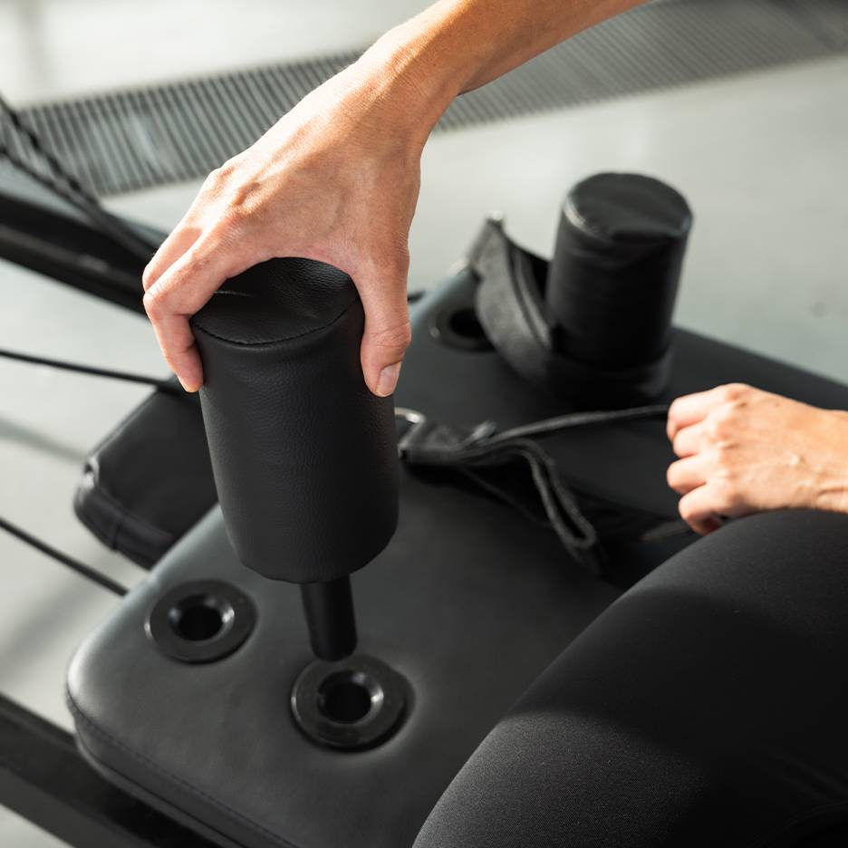 Person adjusting a black padded exercise machine.