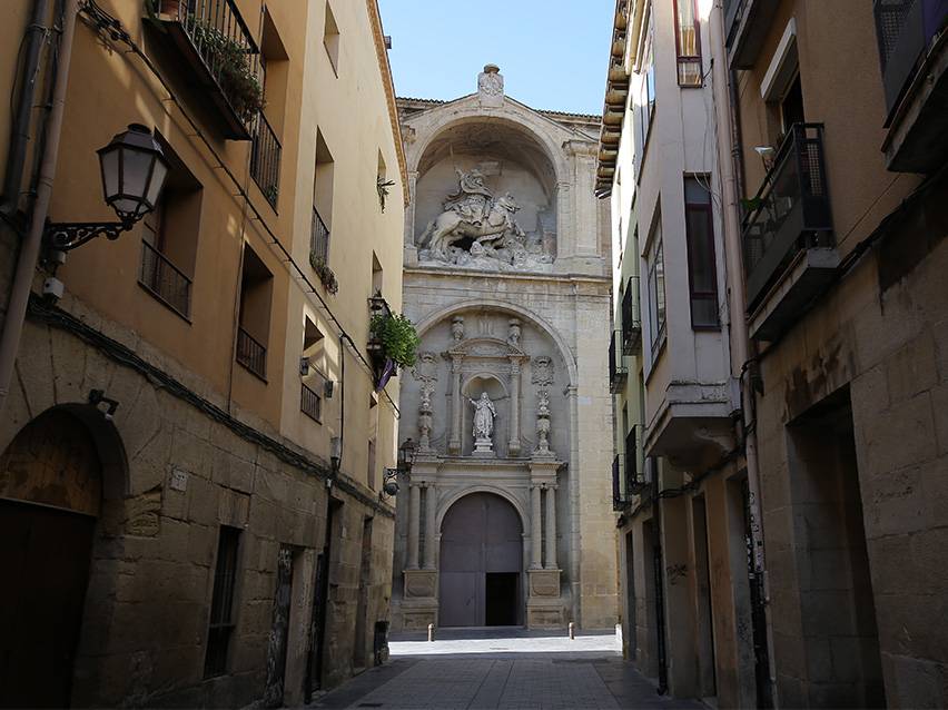 Narrow street leading to a richly decorated church facade with an equestrian statue.