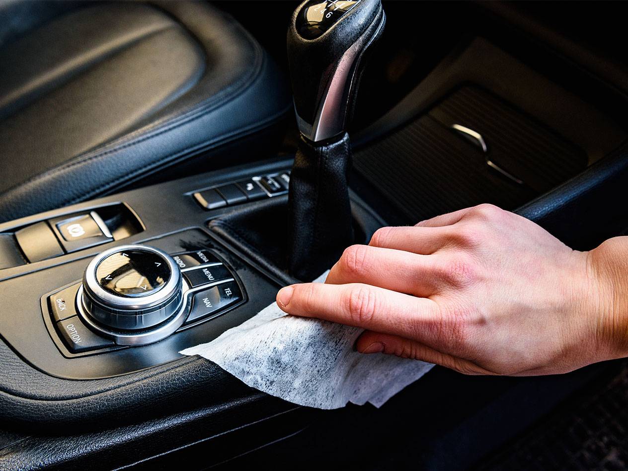 Hand cleaning car interior with a wet wipe.