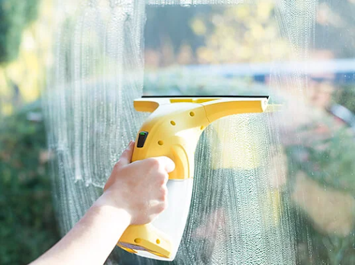 Hand cleaning a window with a yellow electric window cleaner.