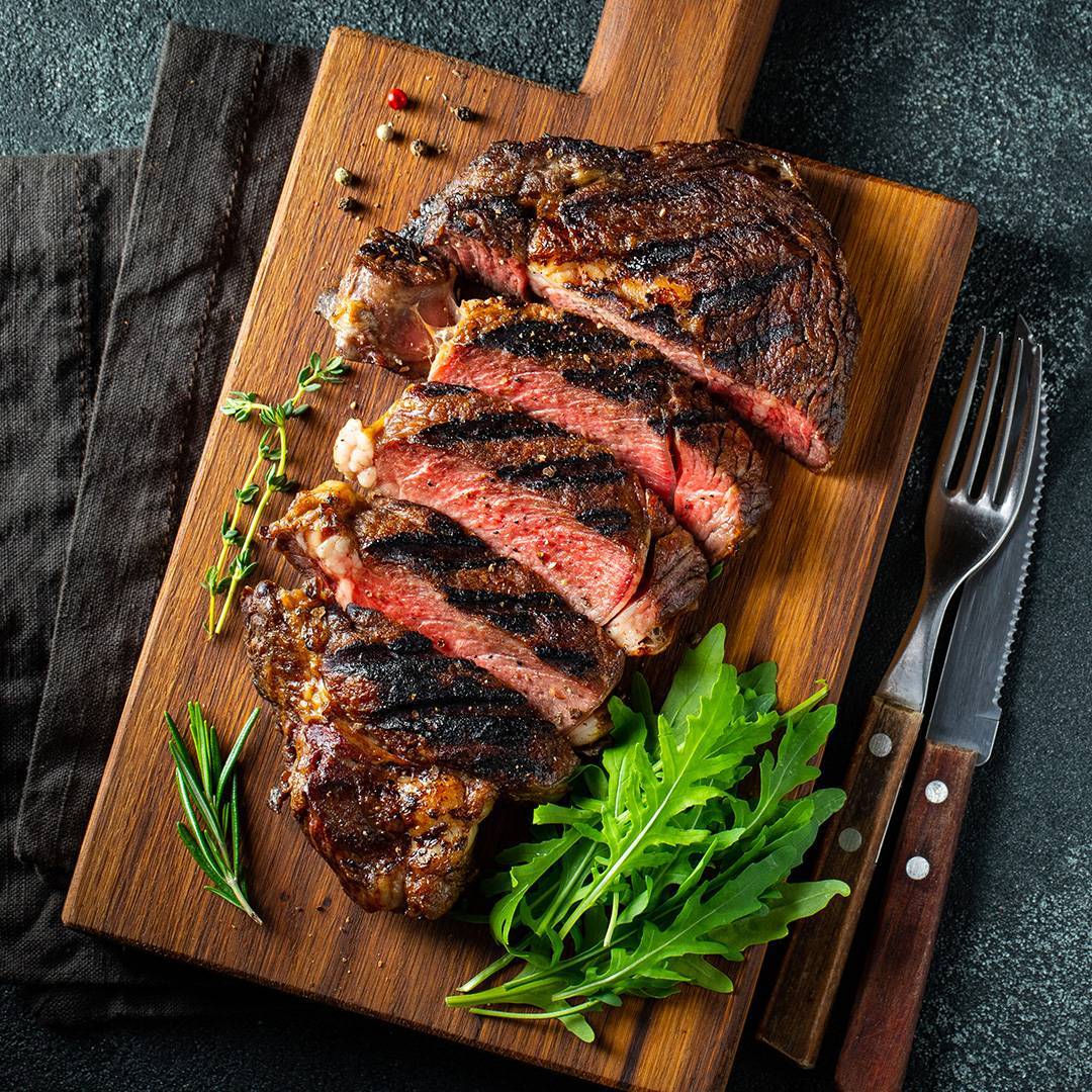 Grilled steak, sliced, with herbs and arugula on a wooden board.