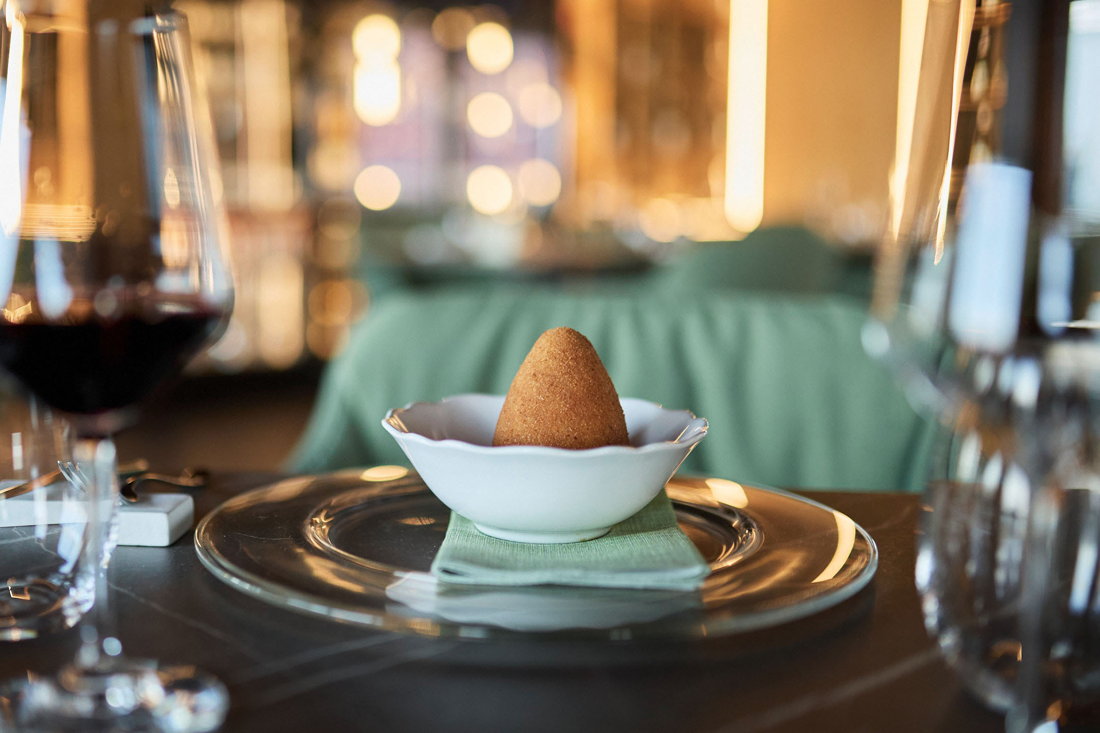 Golden arancini in a white bowl on an elegant restaurant table.