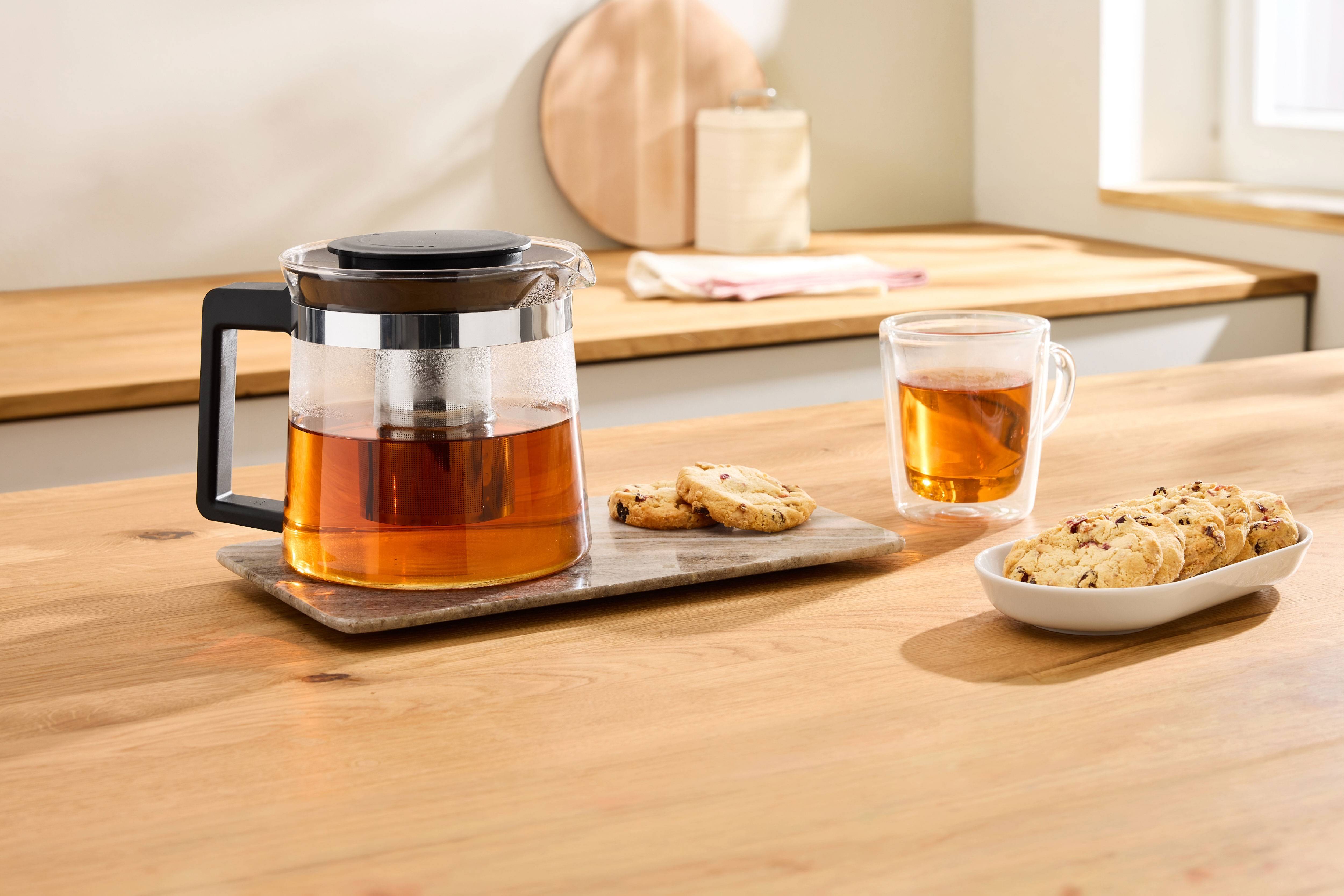 Glass teapot with tea and cookies on a wooden kitchen countertop.