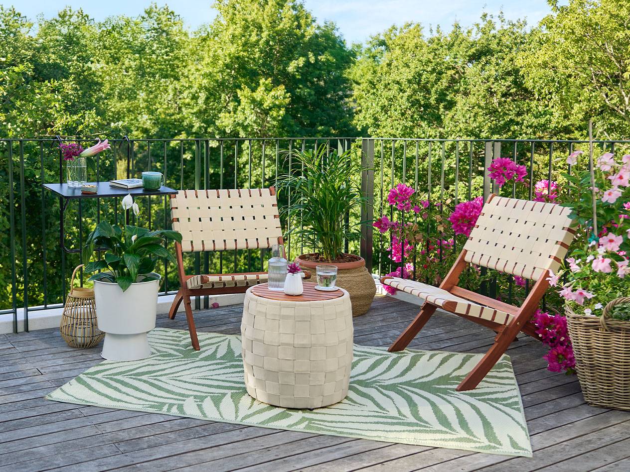 Balcony with wooden flooring, chairs with woven backs, a table, and plants.