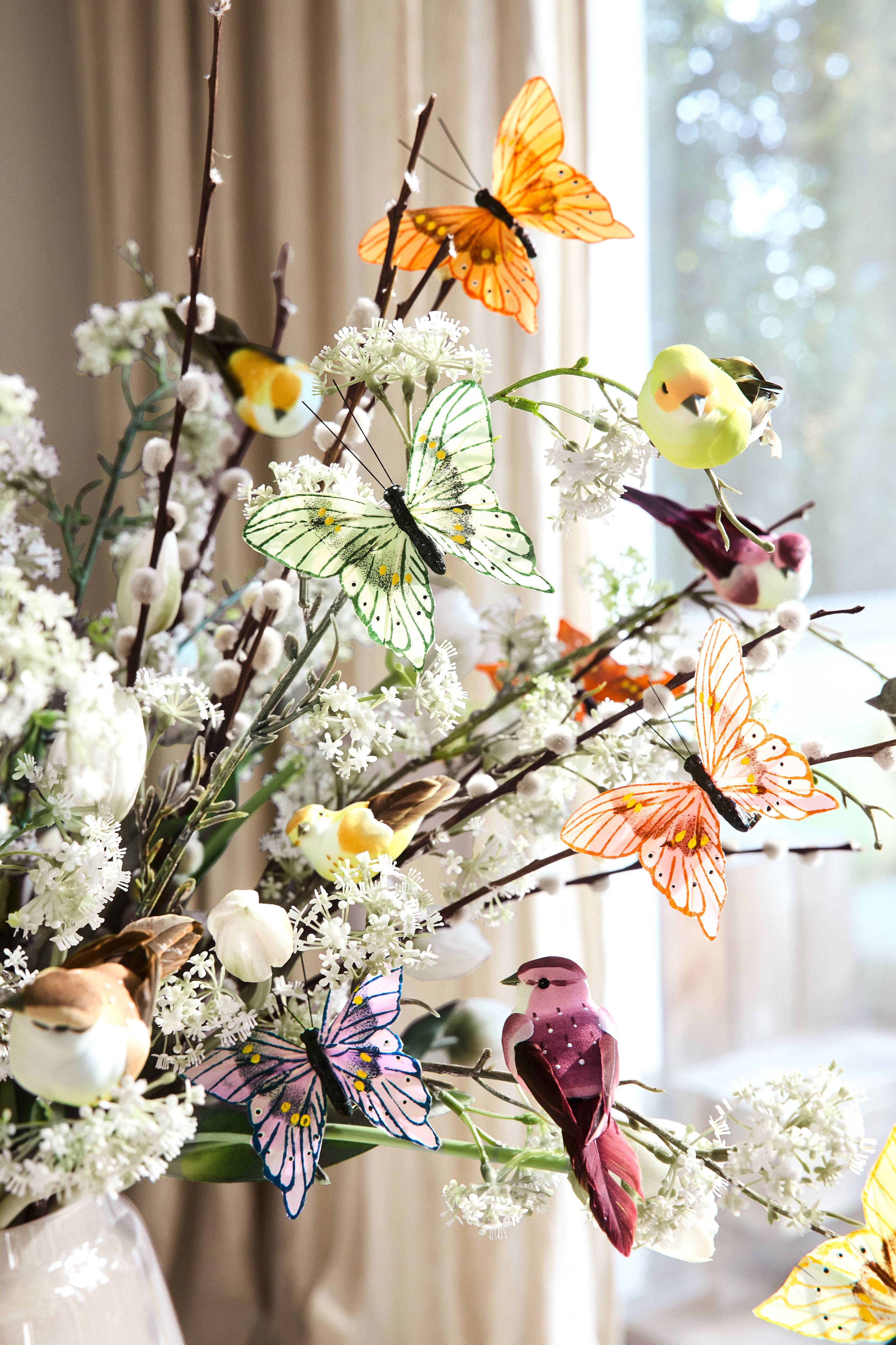 Spring decoration with artificial butterflies, birds, and flowers in a white vase.