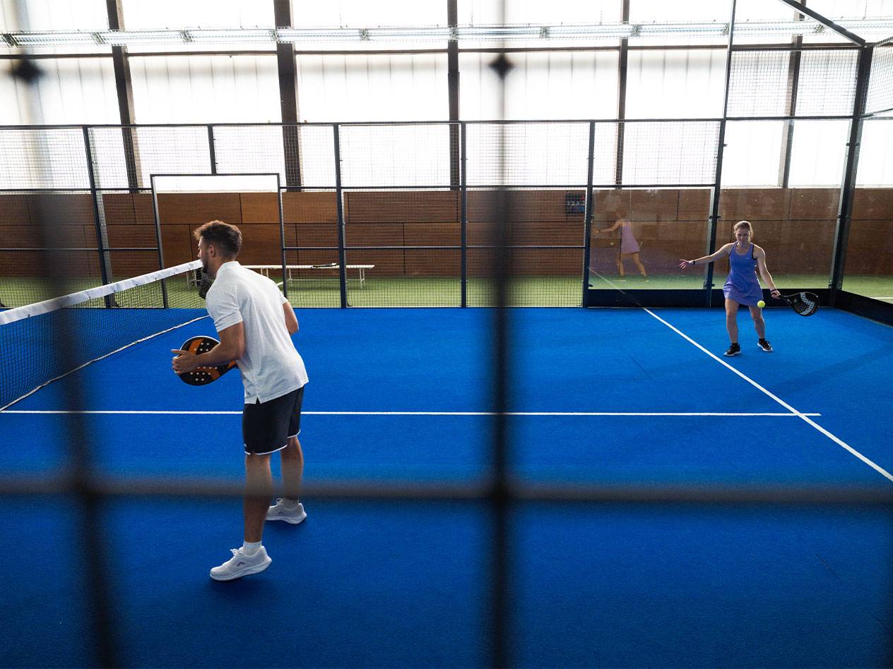 Two people playing padel on a blue court, man holding a racket.