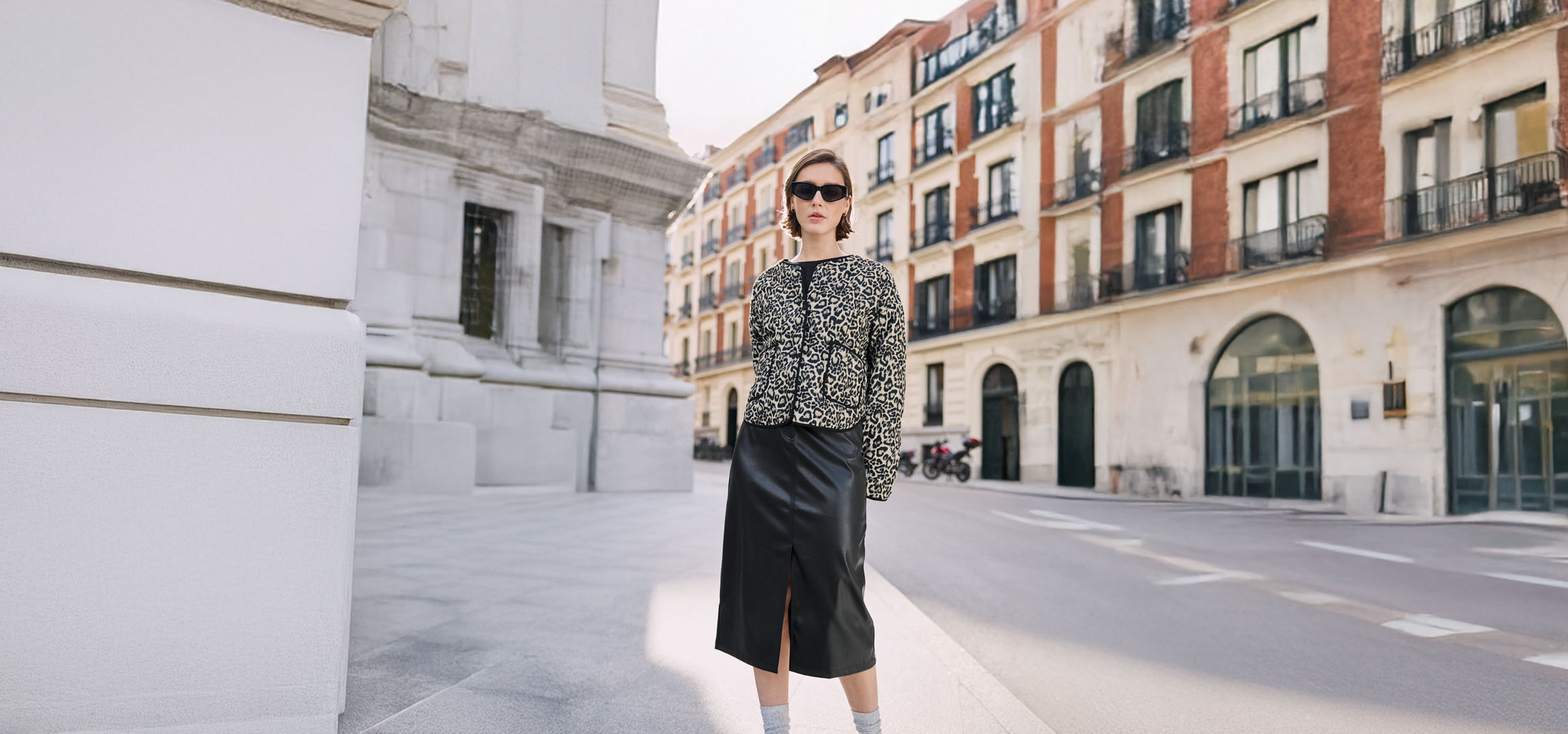 Woman in black skirt and leopard print blouse, on an urban street.