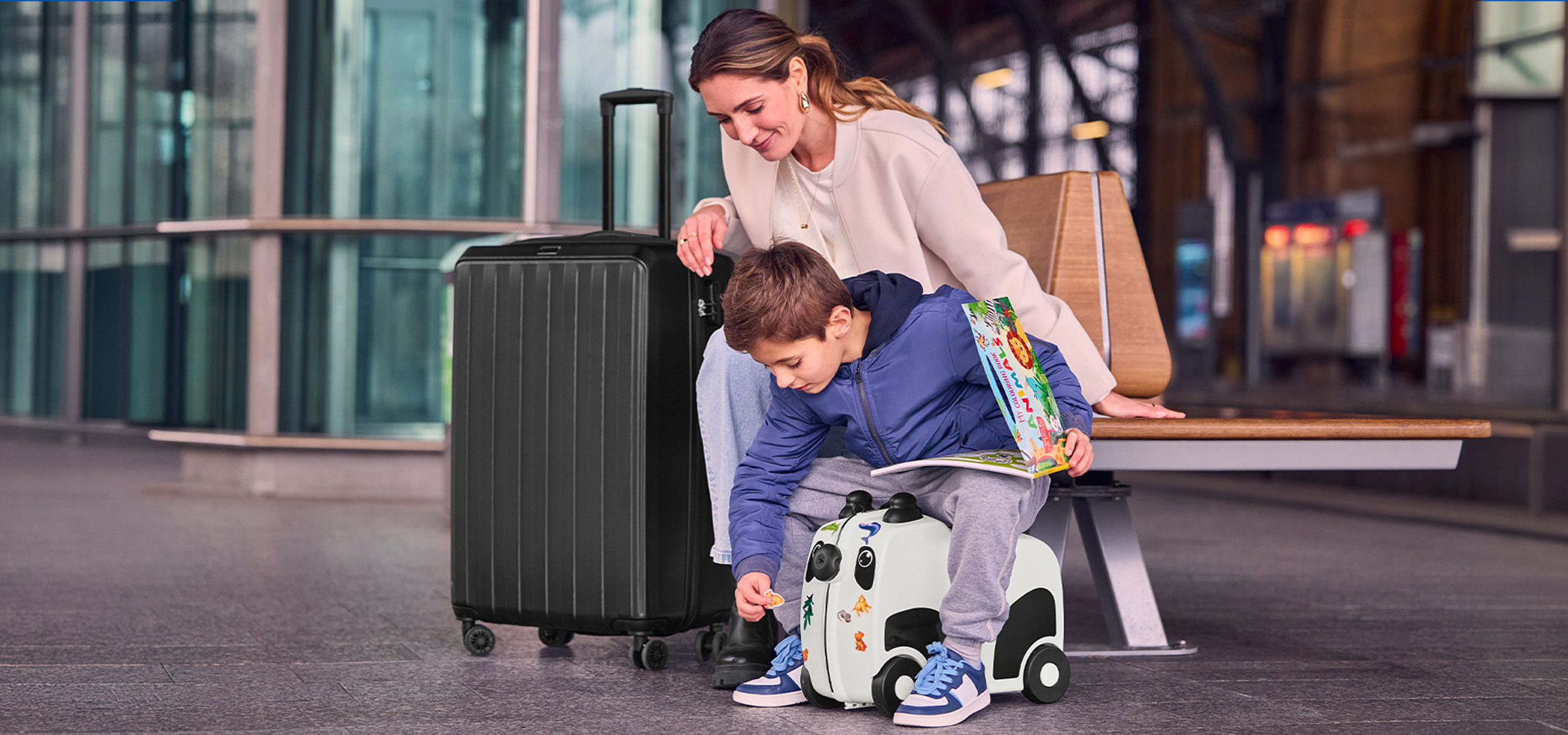 Mother and child with luggage at the airport, child playing with a ride-on suitcase.