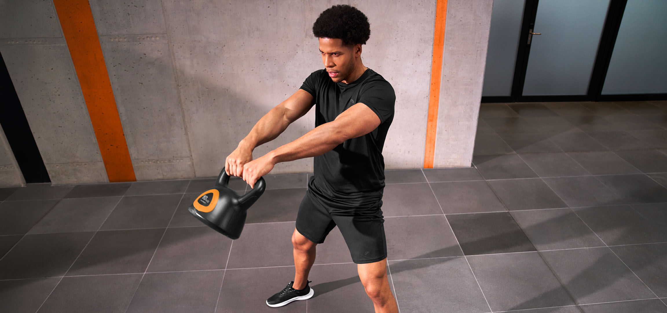 aiLabeling.aiLabelForImageAltText: Man training with a black and orange kettlebell.