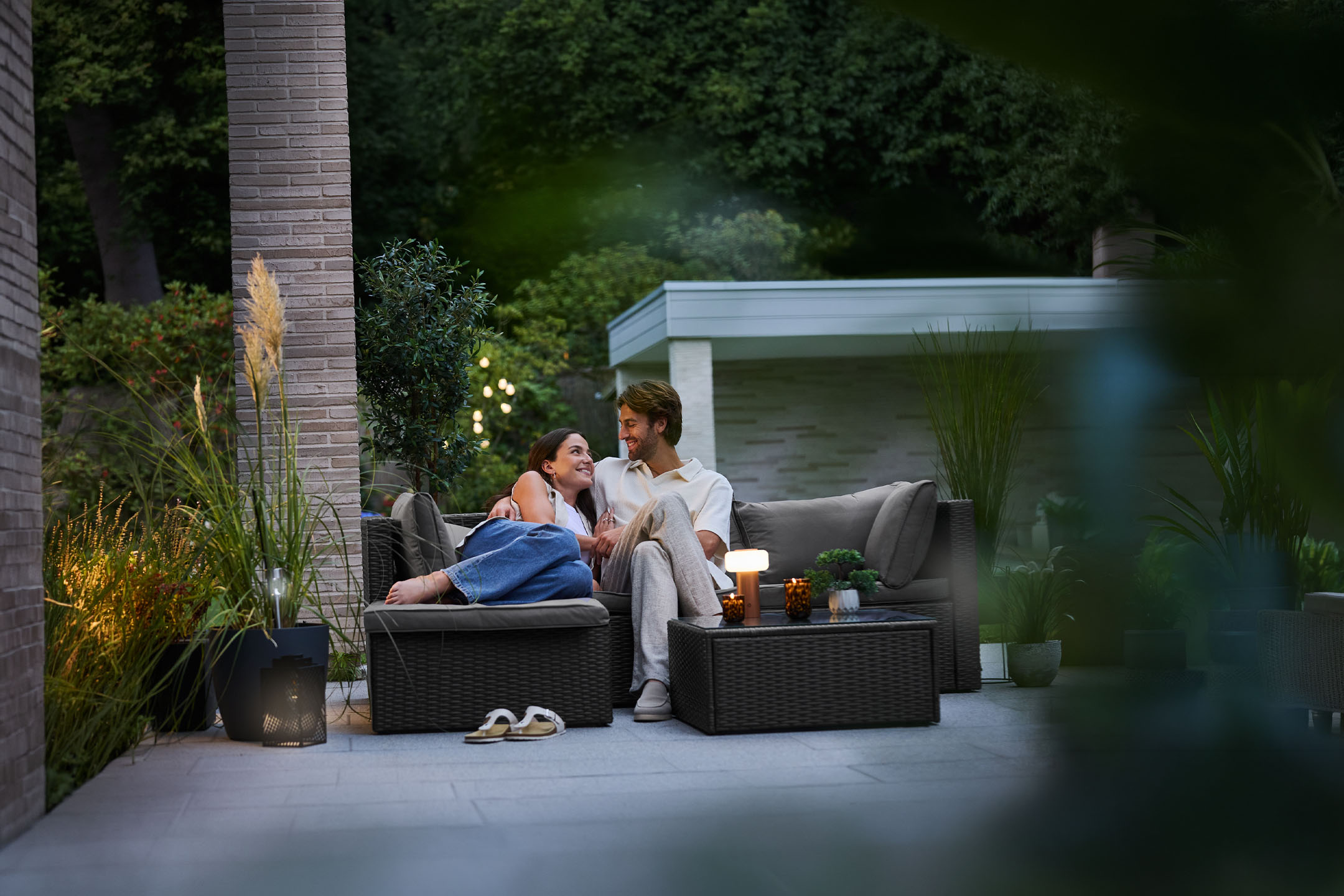 Couple relaxing on rattan garden furniture, illuminated by outdoor lamps.