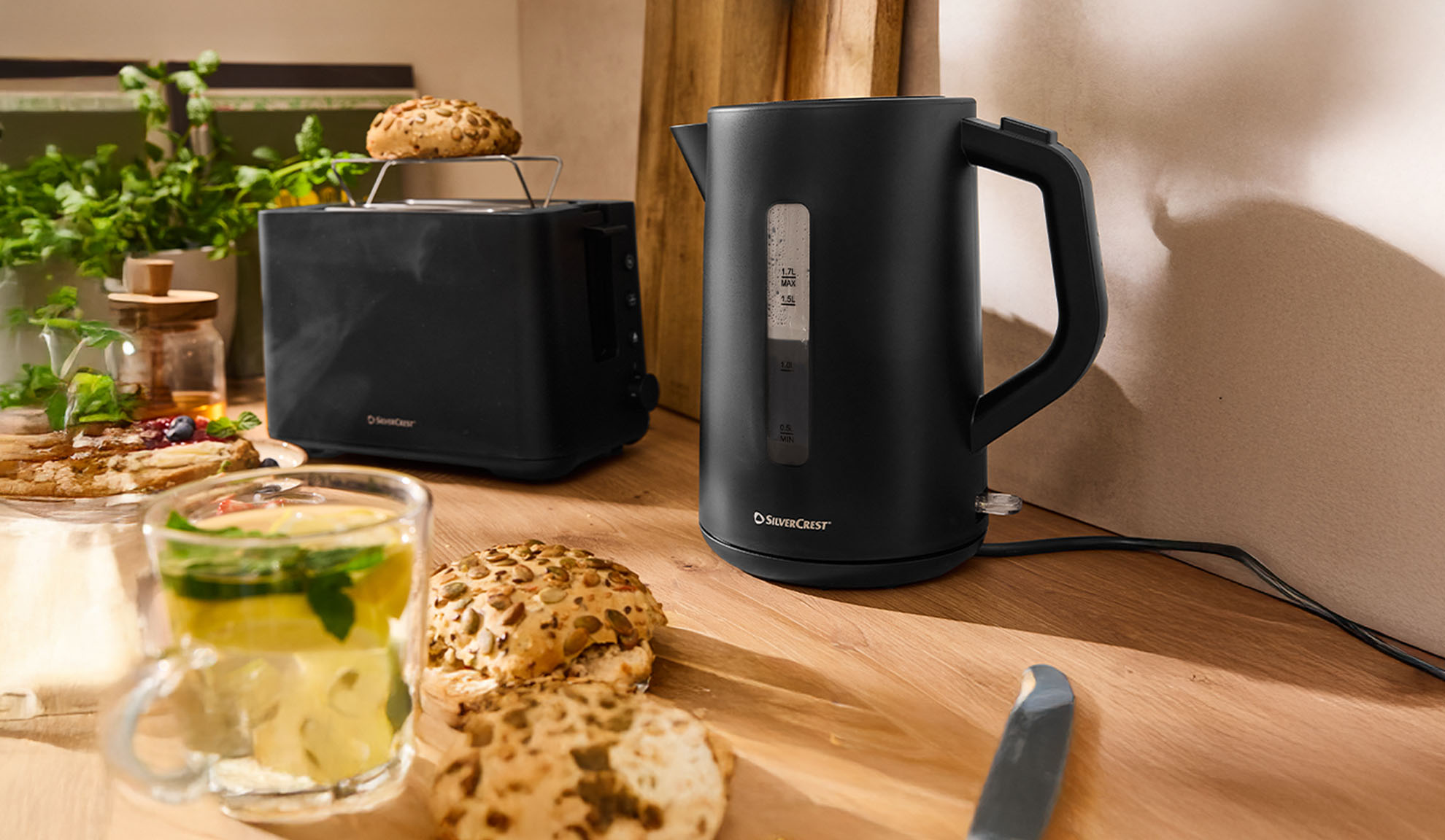 Black SilverCrest kettle and toaster on a wooden table with breakfast.
