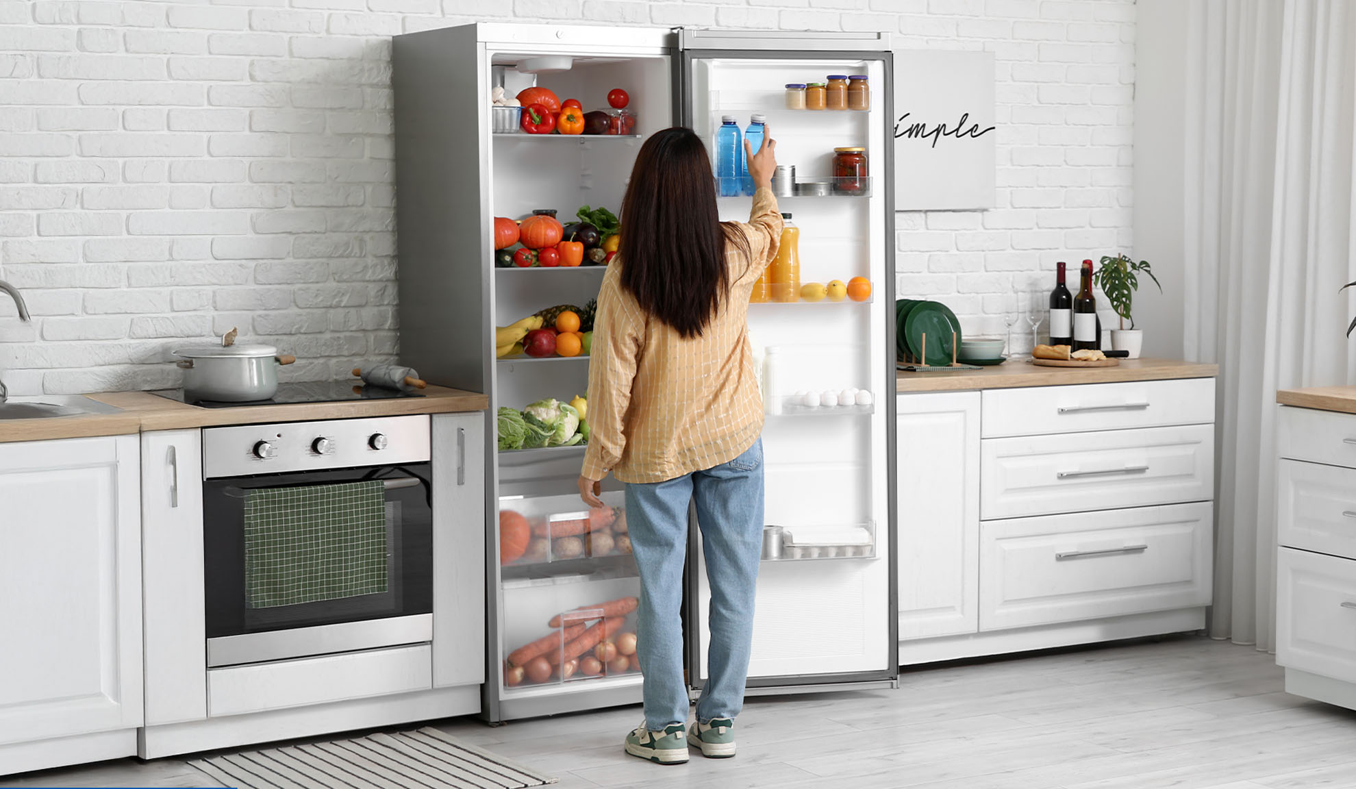 Woman arranging fruits, vegetables, and drinks in a modern kitchen refrigerator.