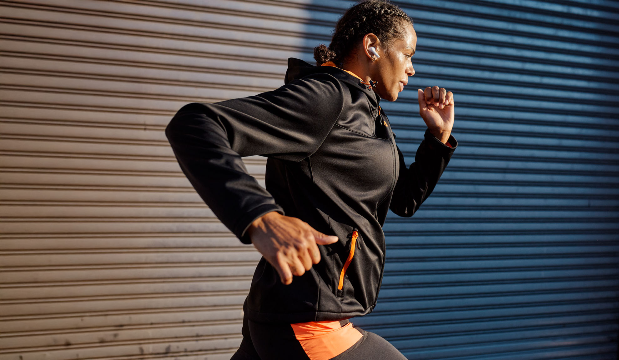 A woman wearing wireless earbuds runs past a metal wall.