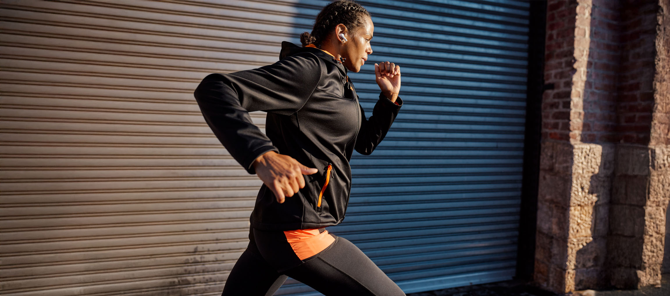 Woman running by a metal wall, wearing earbuds.