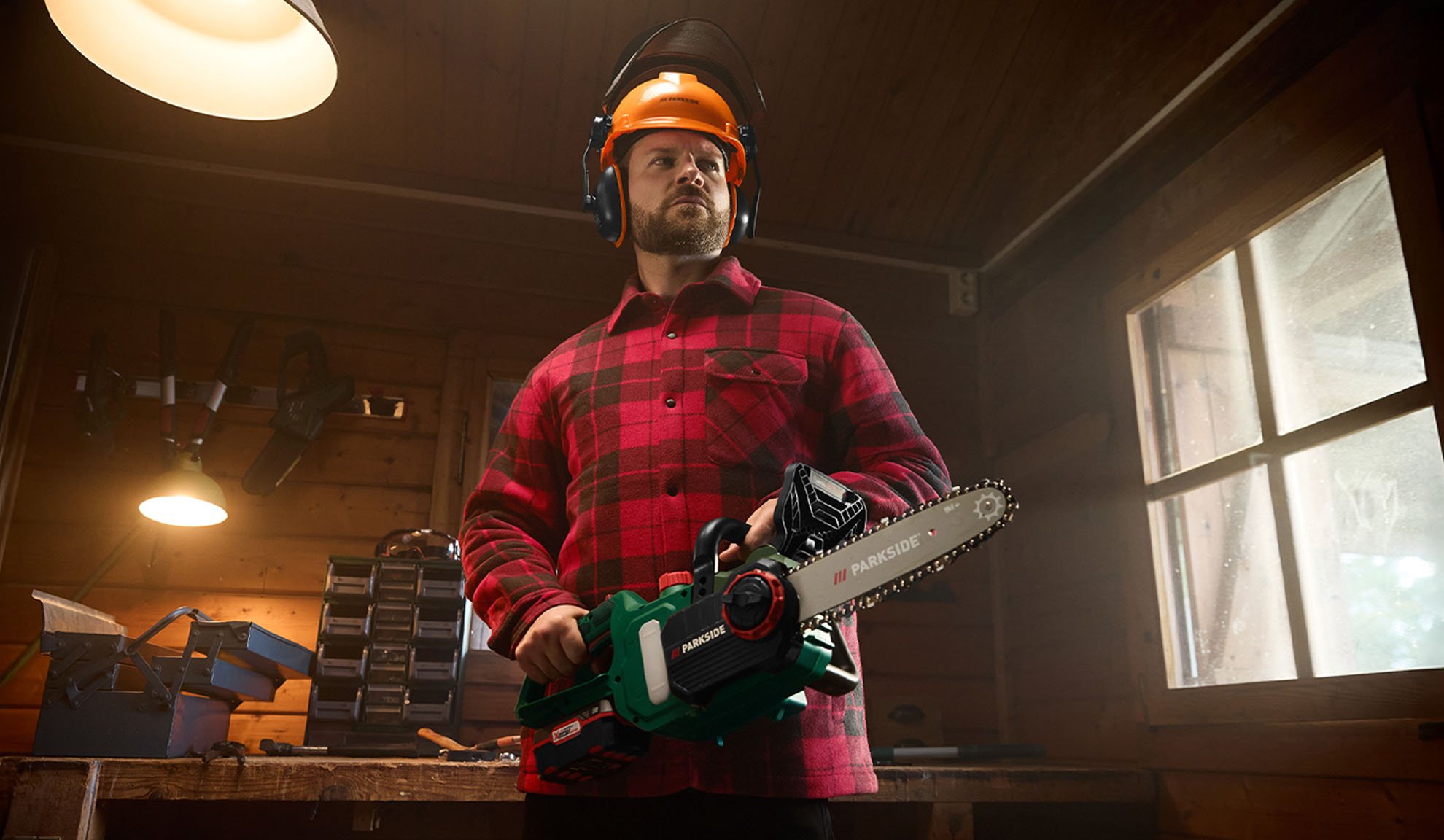 Man in plaid shirt, safety helmet, and Parkside chainsaw in a workshop.