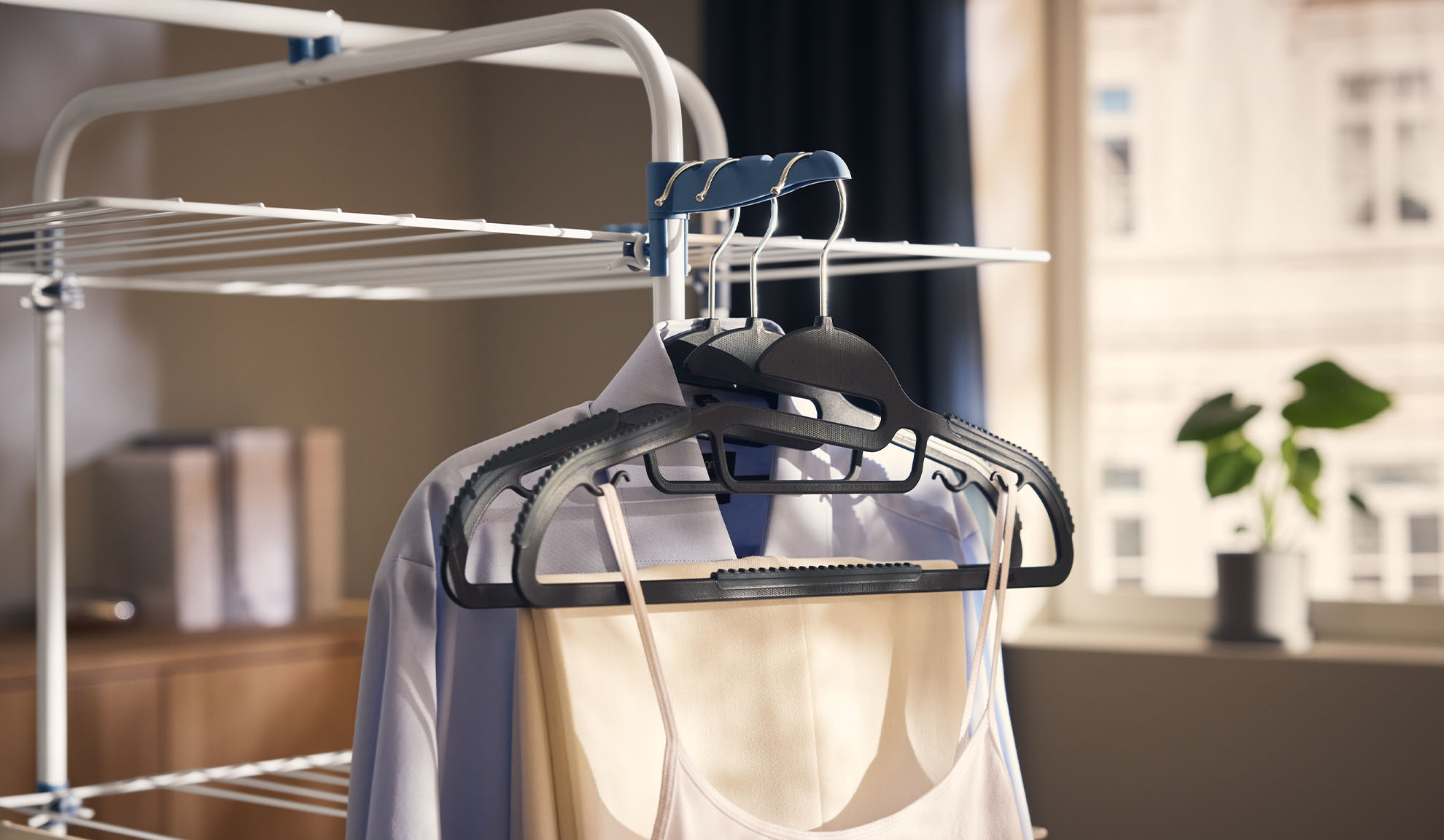 Hangers with clothes on a drying rack, next to a bright window.