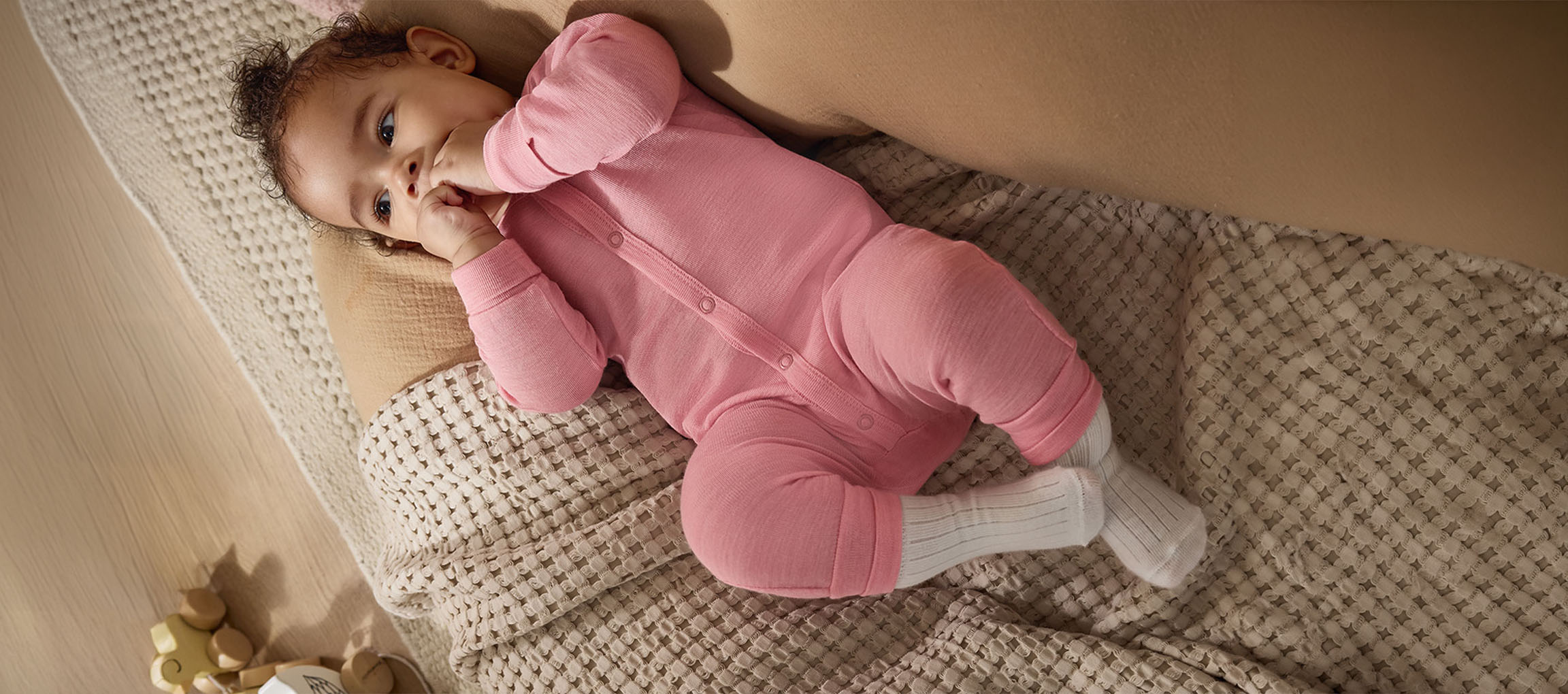 Baby in pink sleepsuit and white socks lying on a textured blanket.