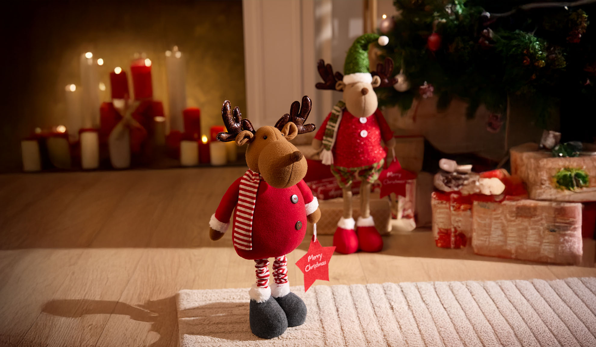 Two Christmas reindeer in red outfits with a 'Merry Christmas' sign, next to a Christmas tree and candles.