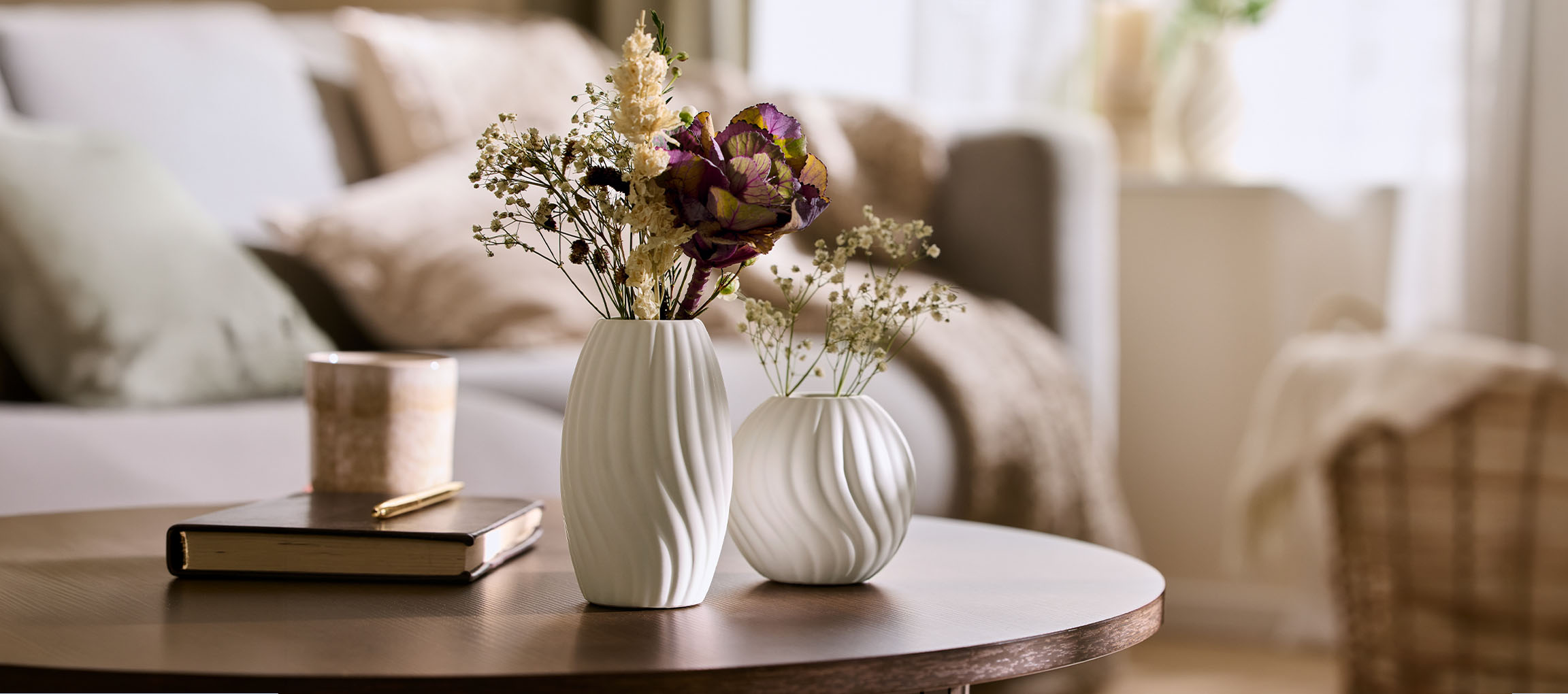 Two white vases with dried flowers on a wooden coffee table in a cozy living room.