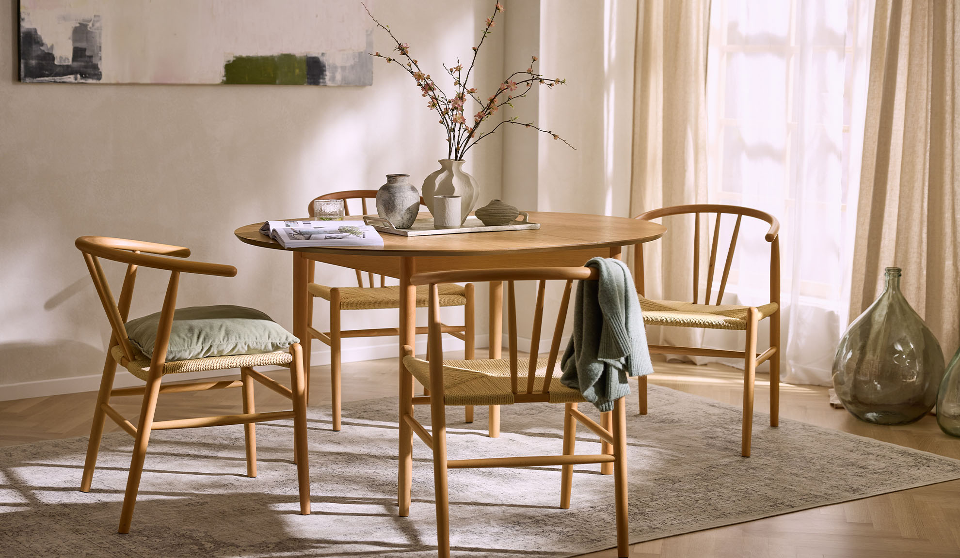 Bright dining area with a round wooden table, wooden chairs with rope seats, and floral decor.