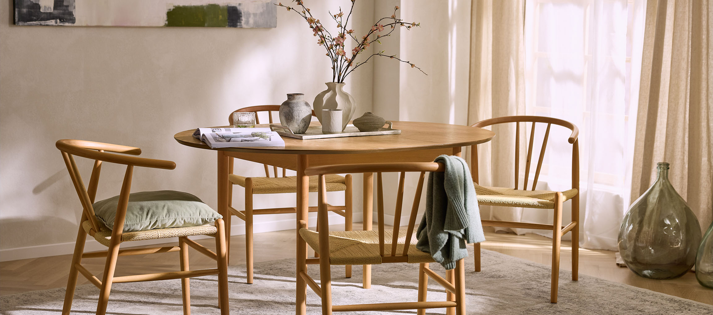 Dining room with a round wooden table, wooden chairs with rope seats, and decorative vases.