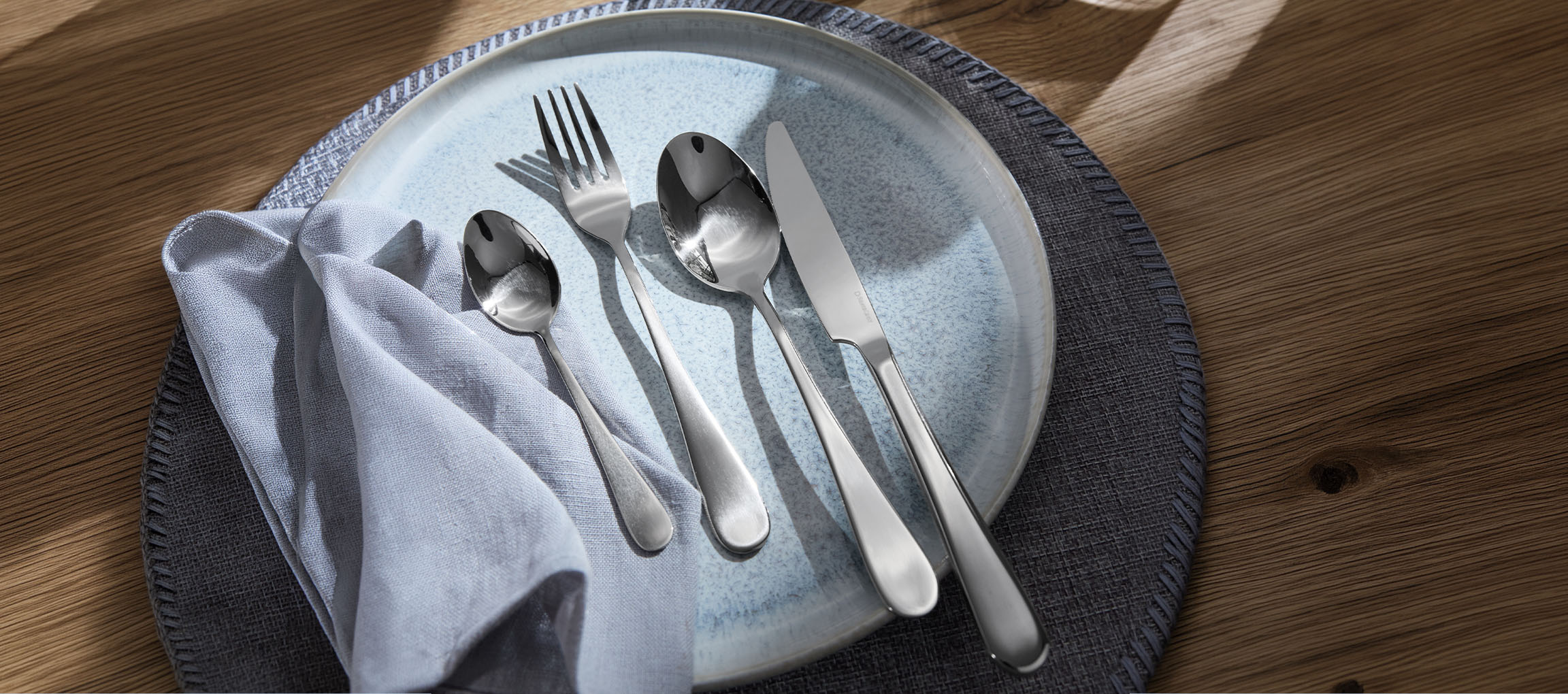Cutlery on a light blue plate with a grey napkin on a wooden table.