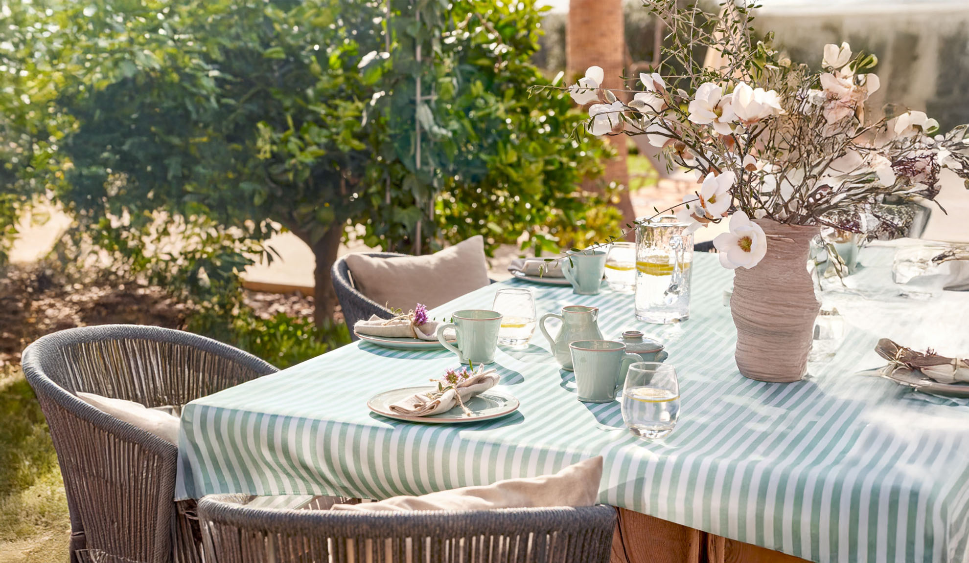 Outdoor dining table with striped tablecloth, ceramic dinnerware, and flower vase.