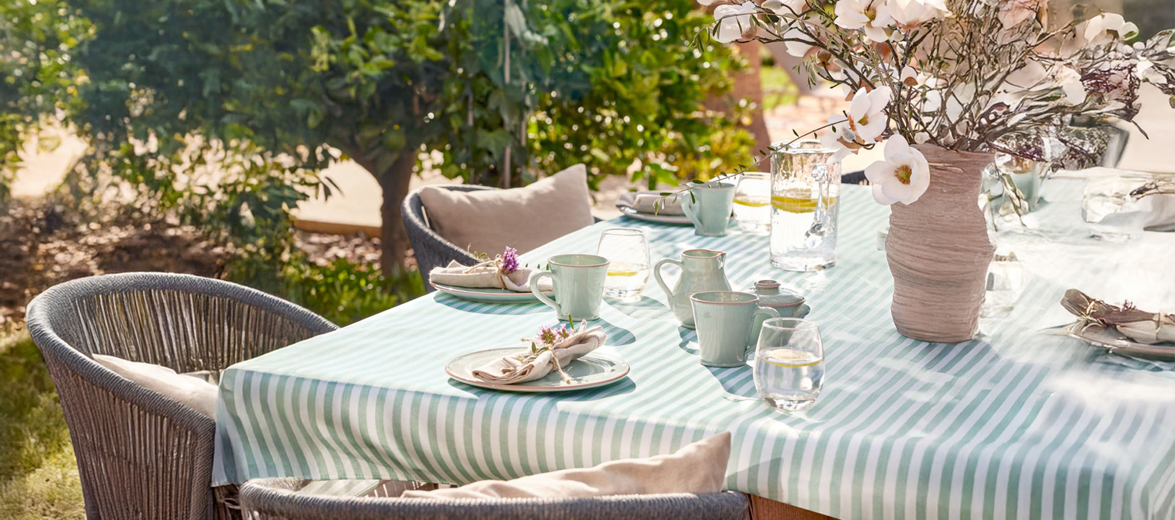 Outdoor dining table set with a striped tablecloth, mint green ceramic dinnerware, and flowers.