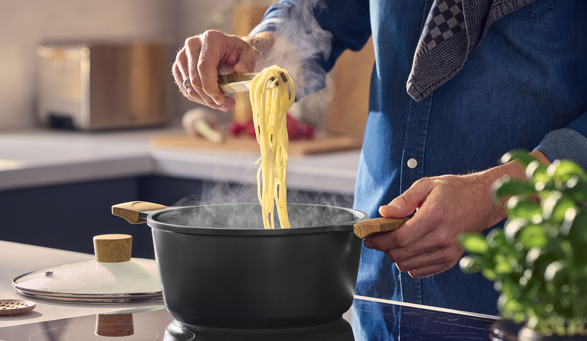 Man lifting steaming spaghetti from a black pot with wooden handles.