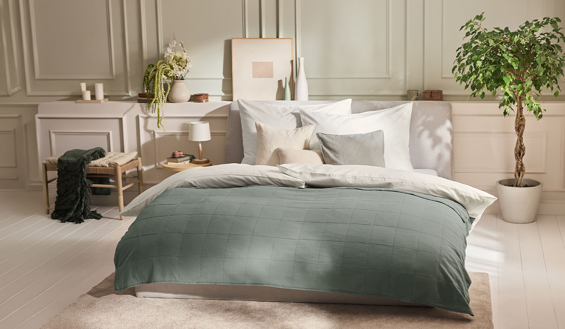 Bedroom with a bed, green duvet cover, white pillows, and a plant