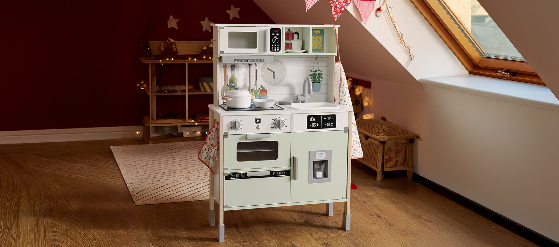 A children's play kitchen in a room with a red wall and wooden floor.
