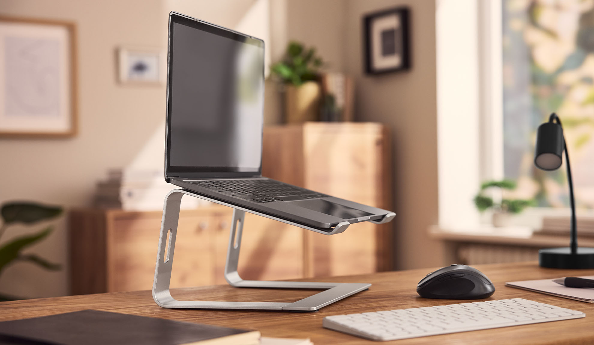 Laptop on a stand, mouse, and keyboard on a wooden desk in a home office.