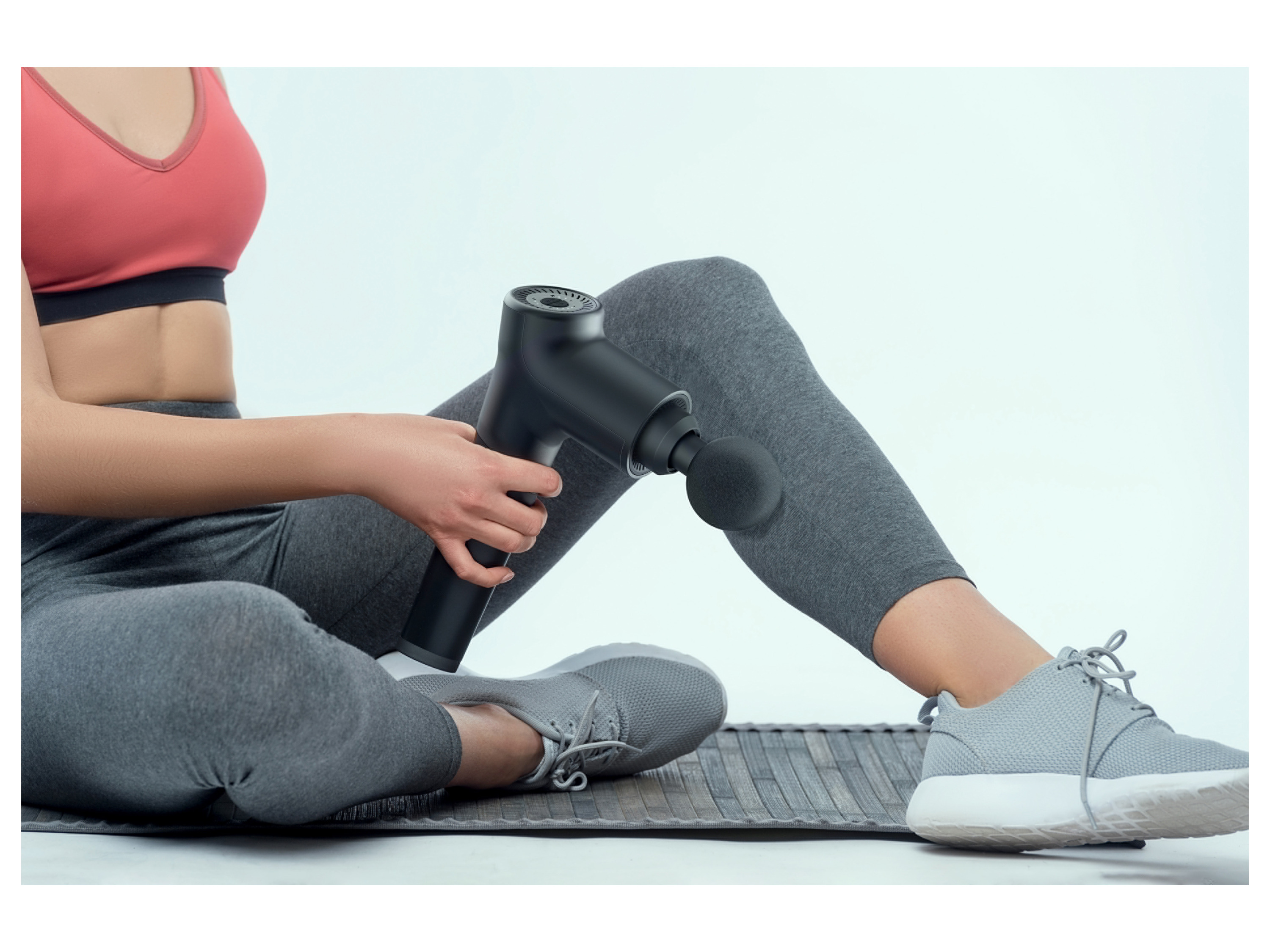 Woman using a percussion massage gun on her leg.