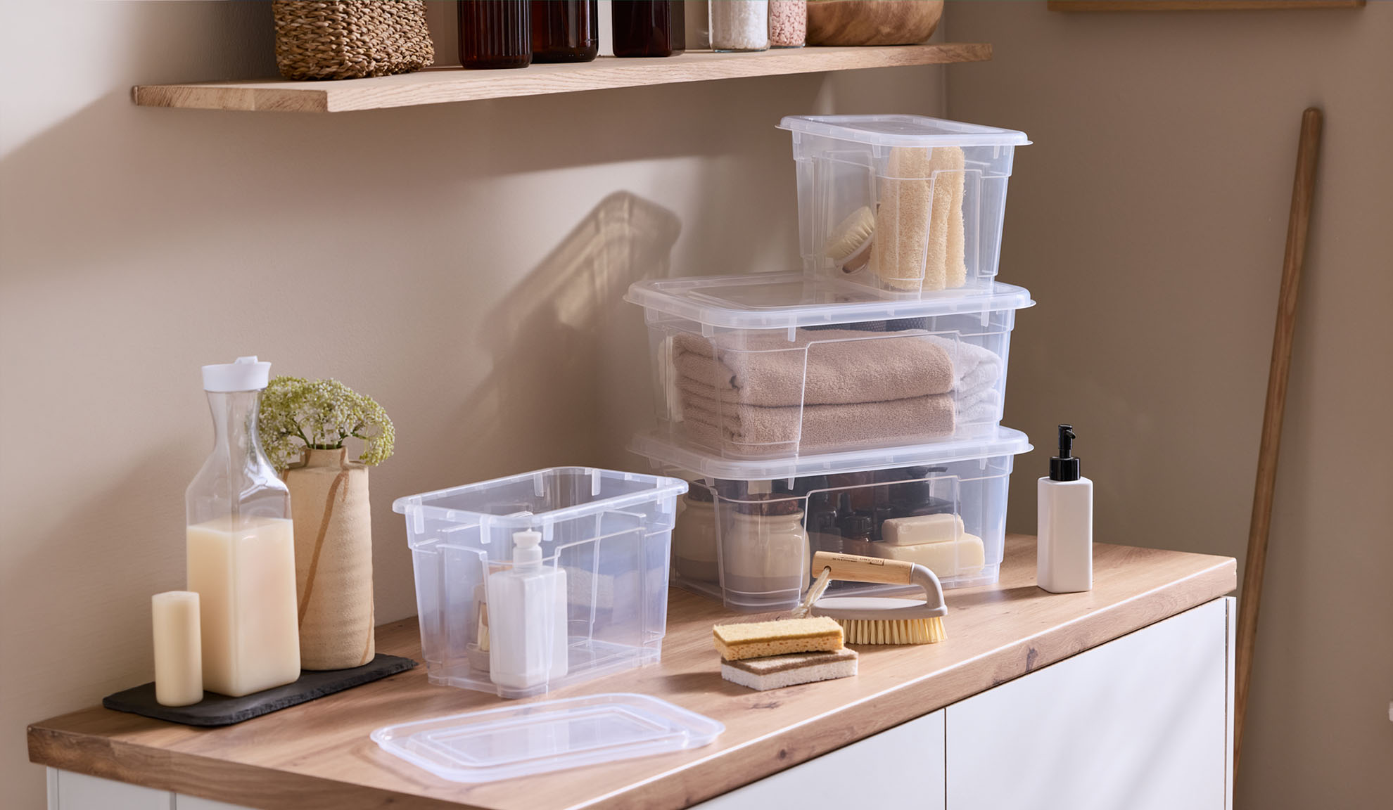 Clear plastic storage boxes with lids, containing towels and bath accessories, on a wooden countertop.