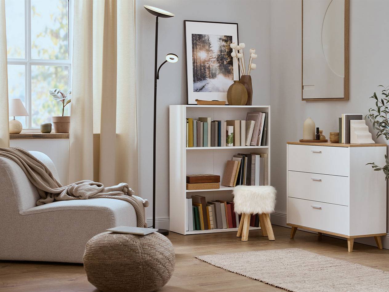 Cozy living room with an armchair, bookshelf, and dresser in neutral colors.