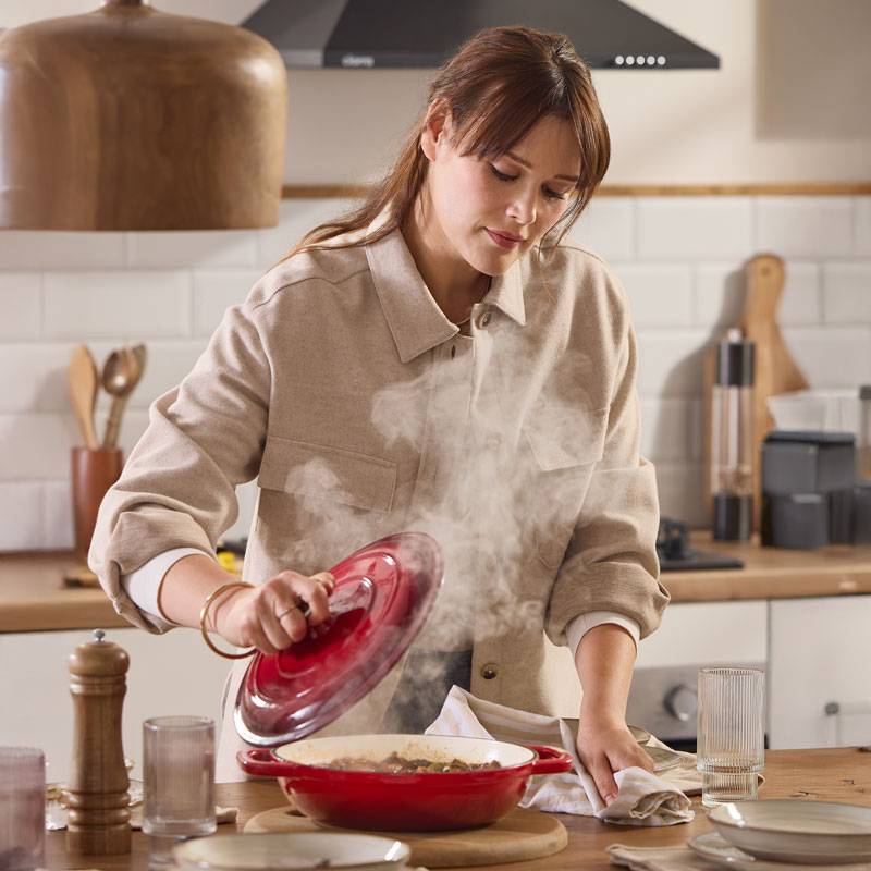 Woman cooking with a red cast iron pot, steam rising from the food.