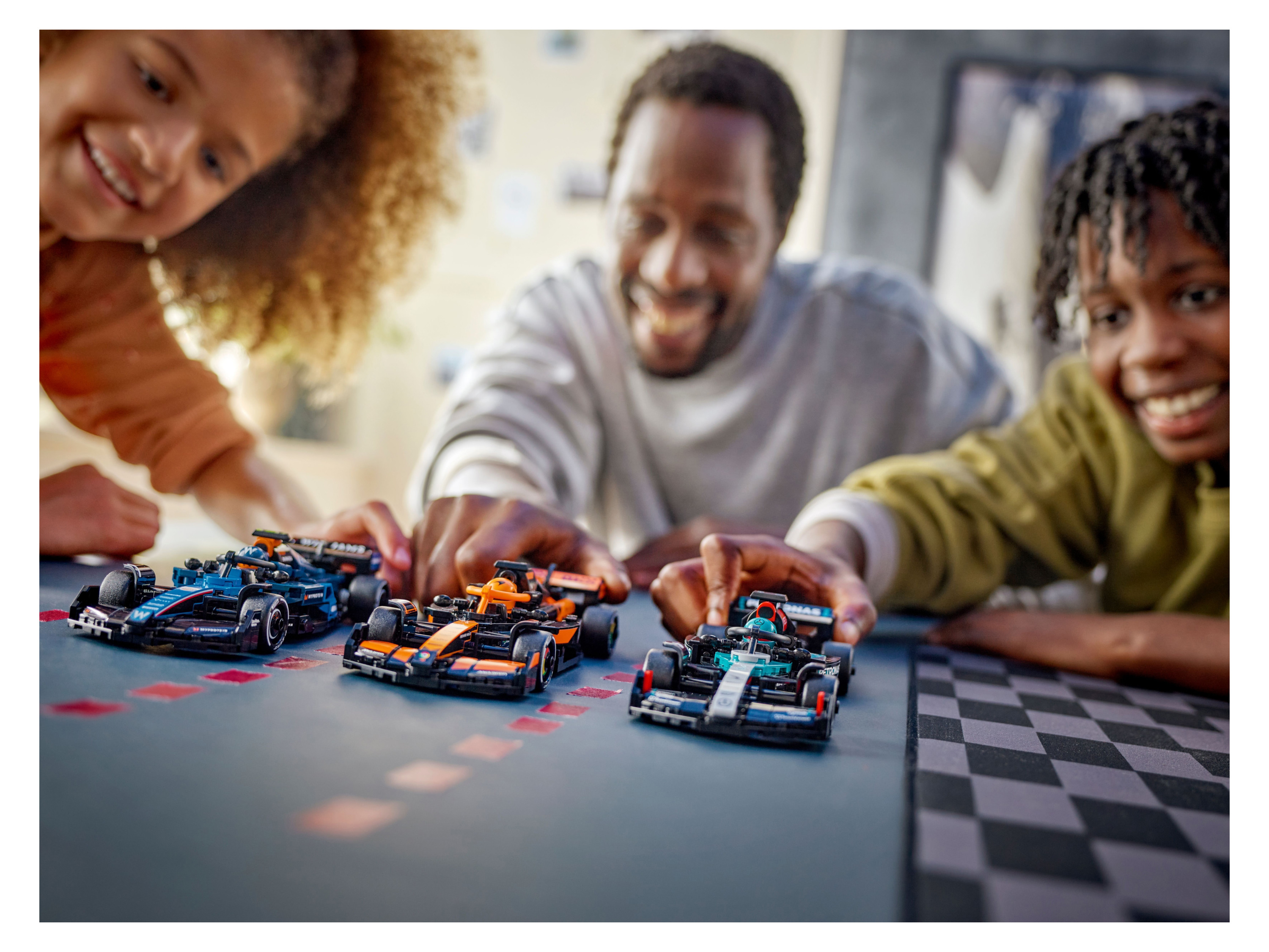 Three people playing with three LEGO Speed Champions race cars on a checkered mat.