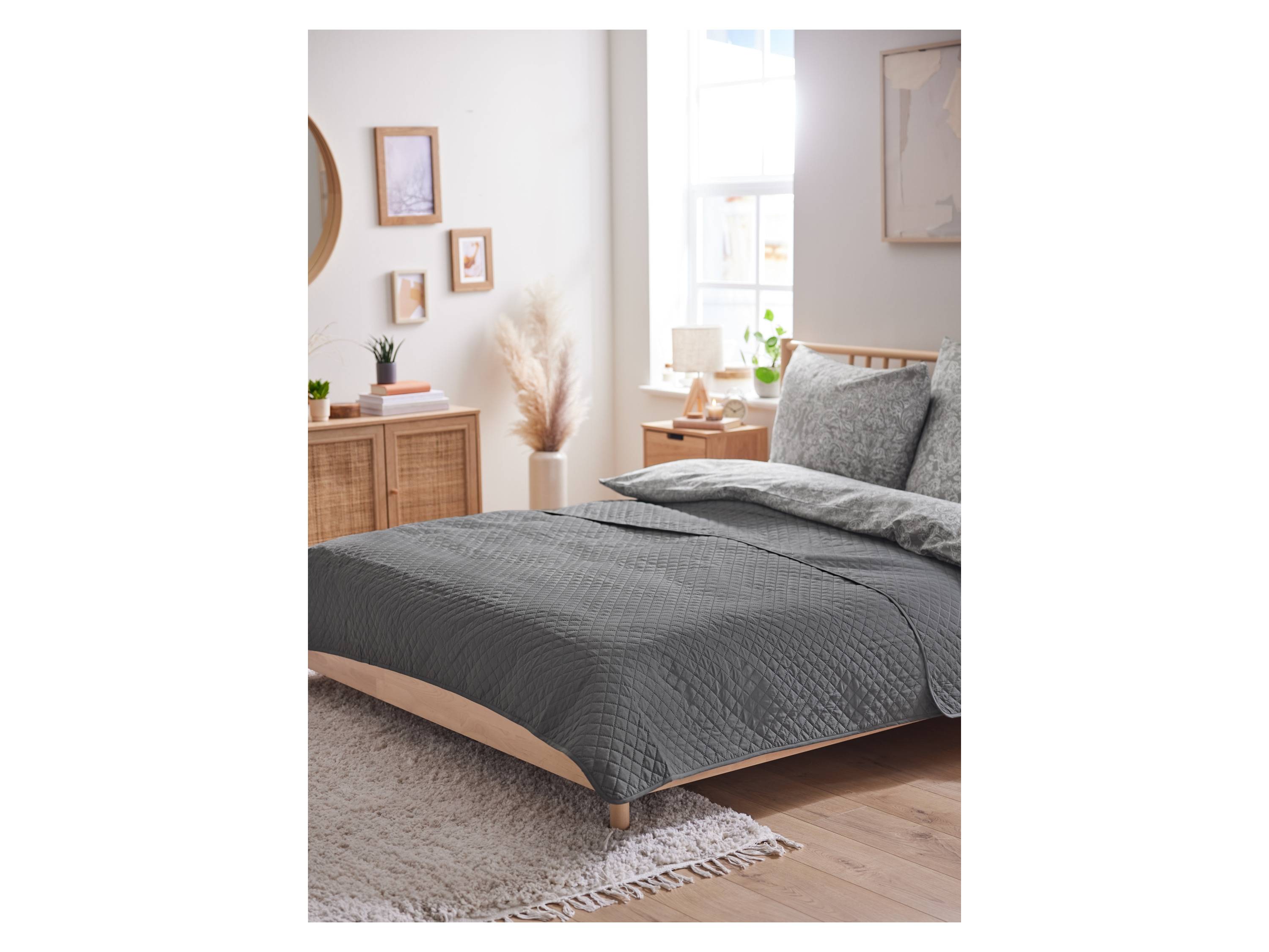 Grey quilted bedspread and floral bedding on a bed.
